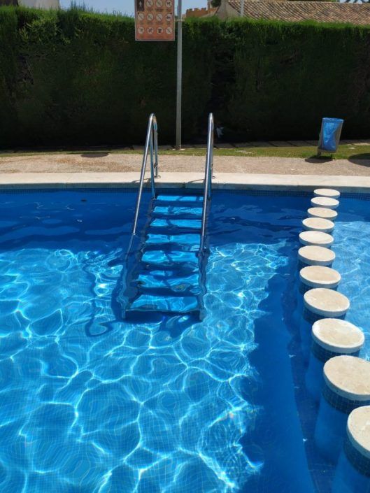 instalacion-escalera-piscina-particulares Detalle de peldaños anchos en acero inoxidable para escalera de piscina comunitaria accesible."